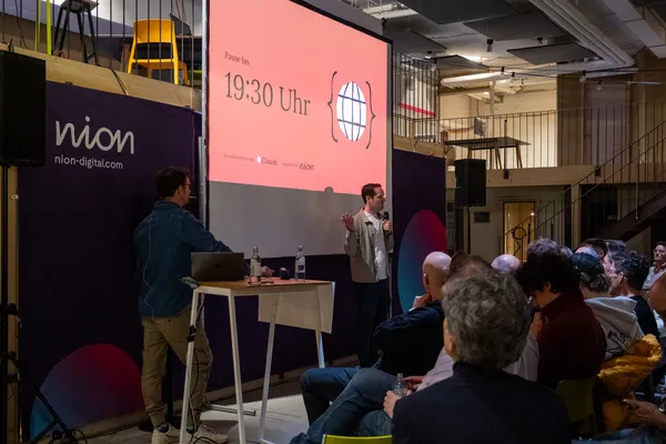 Bühne mit Pausenfolie und Publikum beim ersten Claude Code Meetup