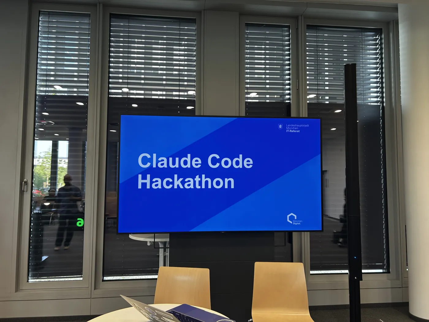 Raum im IT-Rathaus mit dem Bildschirm „Claude Code Hackathon“ vor dem Start des Impact Labs