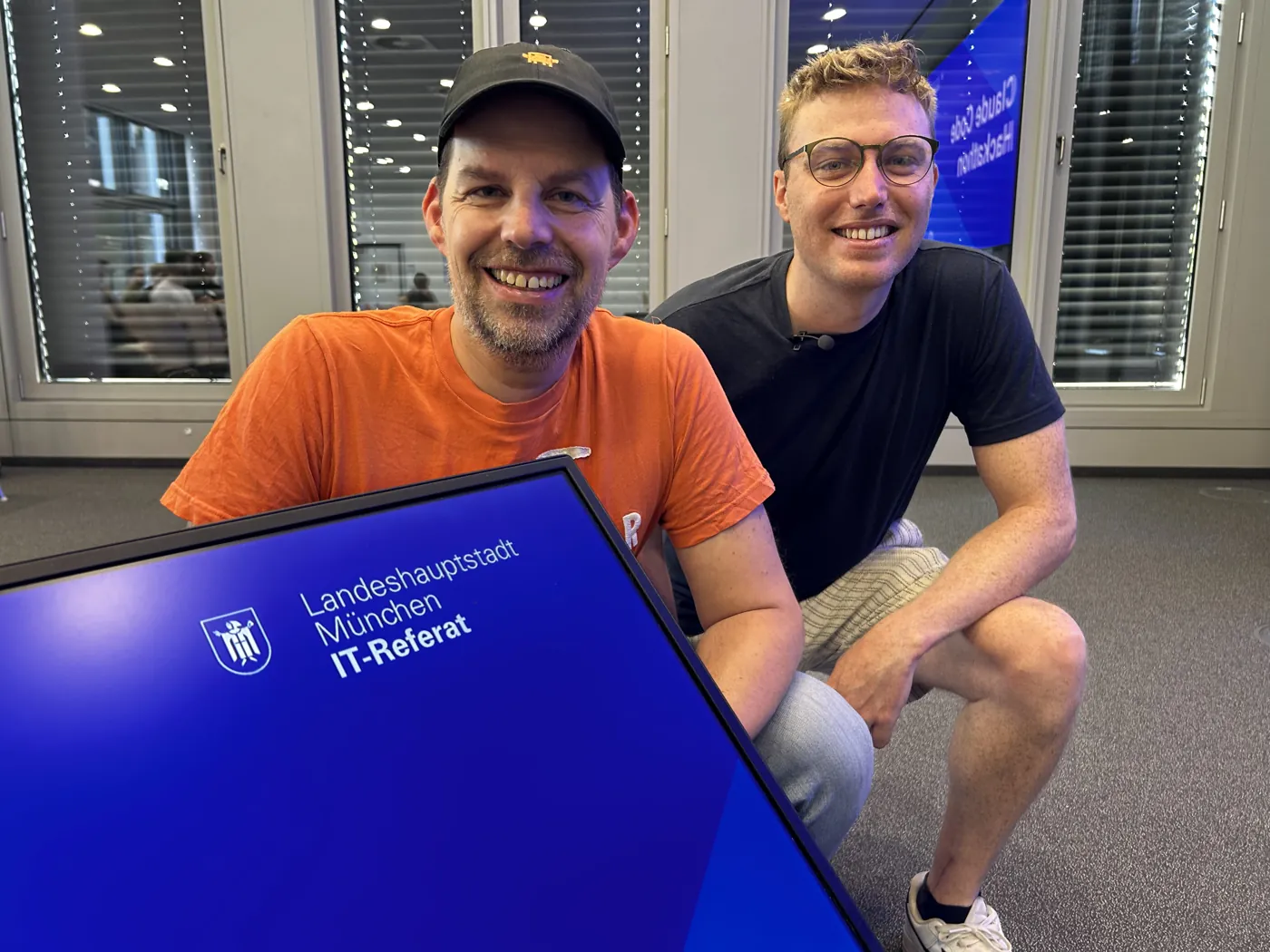 Florian Steiner und Michael Whelehan mit dem Schild der Landeshauptstadt München, IT-Referat