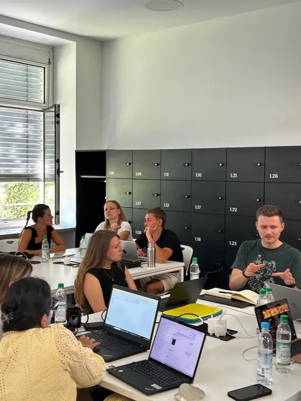 Team mit Laptops an einem Tisch vor einer Wand aus Schließfächern